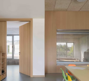 Spazio interno con pavimento chiaro, soffitti lineari e ampie aperture che collegano visivamente l’ambiente educativo all’esterno.