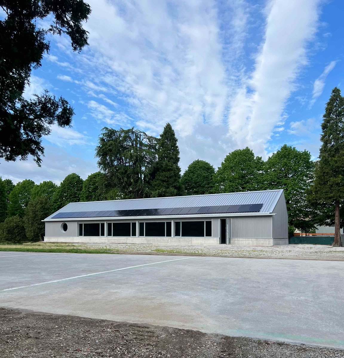 Foto esterni della nuova mensa scolastica alla Scuola Primaria "E. De Amicis" a Villa del Conte (PD), progettata da MD41, edificio moderno e sostenibile nel cortile scolastico.