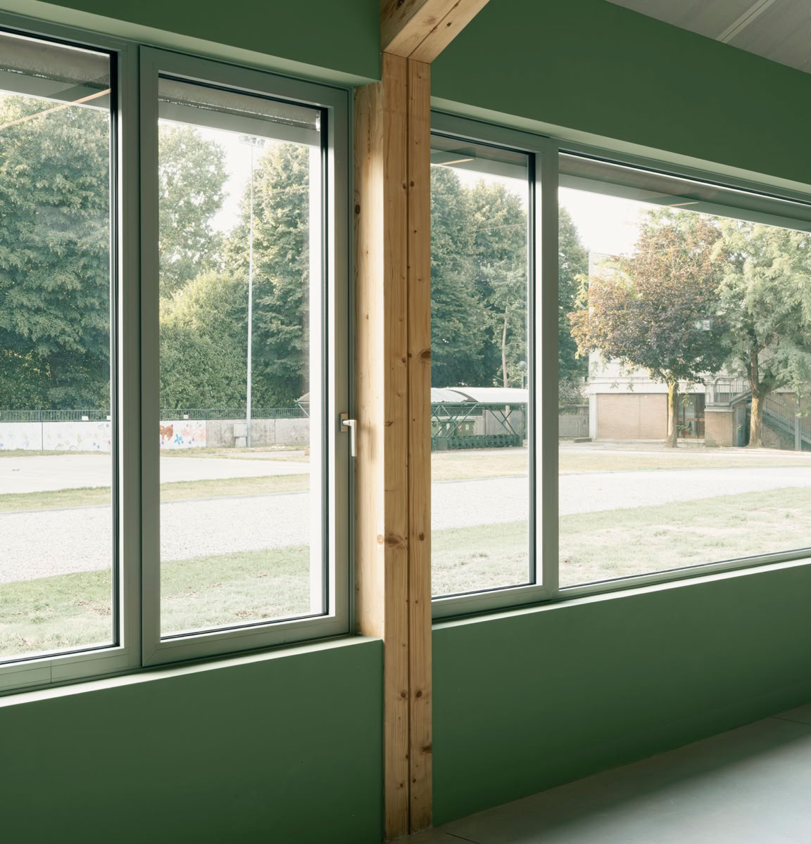 Interno della mensa scolastica di Villa del Conte con pareti verdi e grandi finestre che mostrano un paesaggio esterno con alberi.