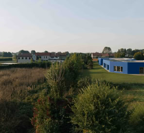 Vista dell’esterno della scuola dell’infanzia di Noventa Vicentina, con la facciata blu compatta, angoli curvi e ampie aperture rivolte verso il giardino a Est.